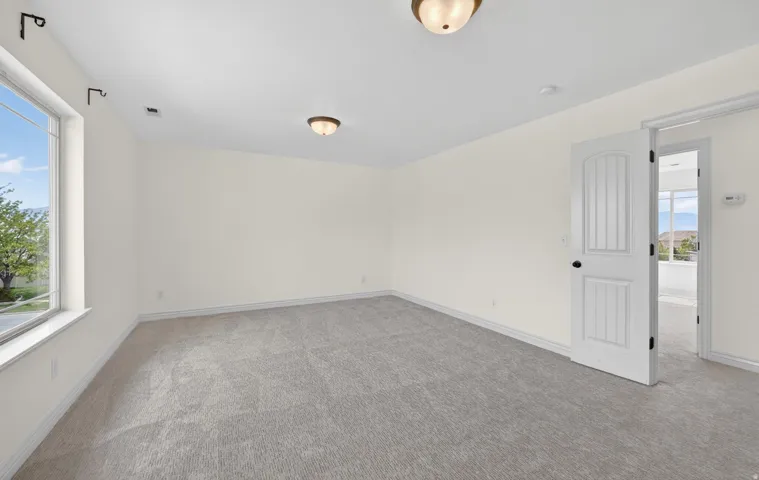 Spacious room featuring neutral carpeting, light-toned walls, and a large window providing natural illumination