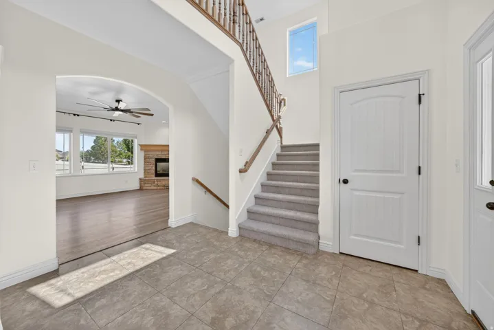 Foyer featuring tile flooring, a carpeted staircase with wood banister, and an arched entryway opening to a living area with wood-finish flooring, a stone fireplace, and multiple windows