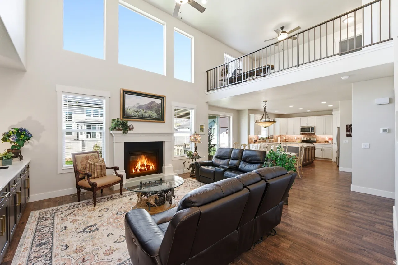 Living room with dark wood-type flooring, a glass covered fireplace, a ceiling fan, a high ceiling, and recessed lighting