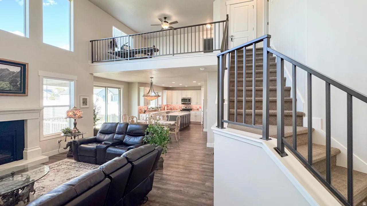 Living room featuring a ceiling fan, a fireplace with raised hearth, a high ceiling, dark wood finished floors, and recessed lighting