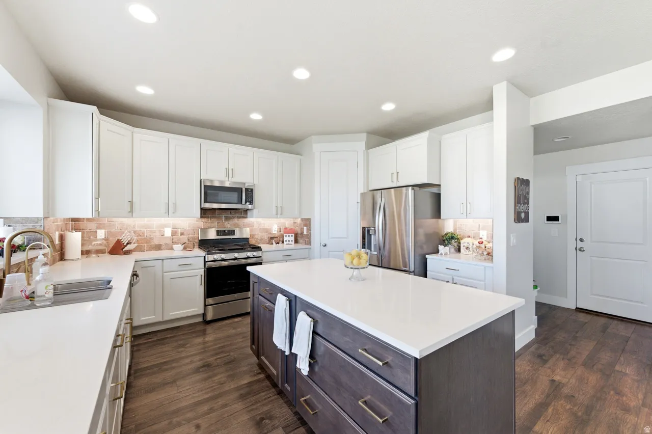 Kitchen featuring stainless steel appliances, dark wood finished floors, a center island, two tone cabinets, and tasteful backsplash