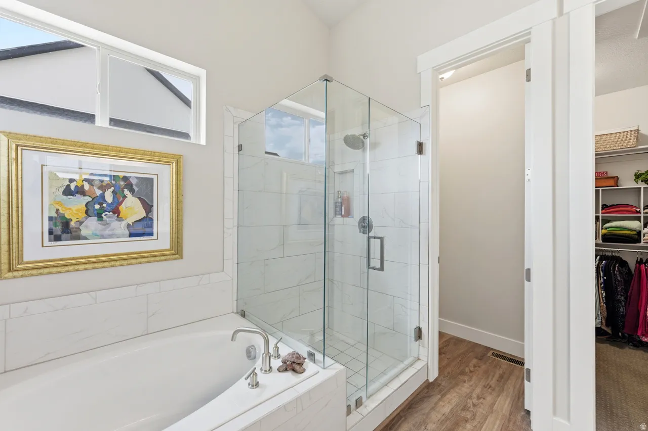 Full bath with a shower stall, a bath, a spacious closet, and light wood finished floors