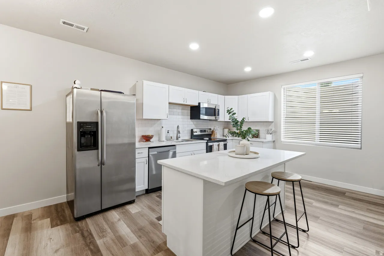 Kitchen with stainless steel appliances, white cabinetry, a kitchen bar, a kitchen island, and light wood-style flooring