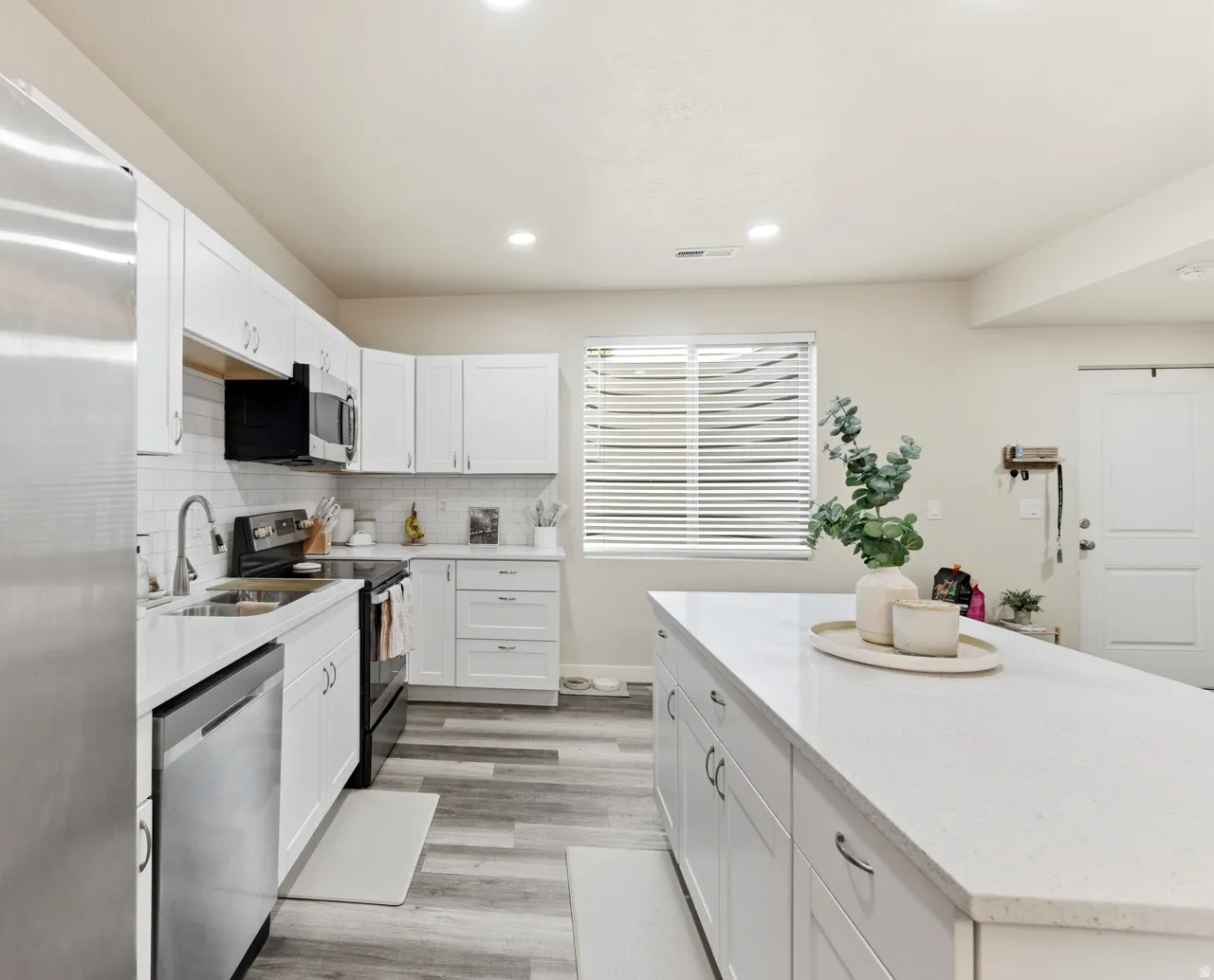 Kitchen featuring stainless steel appliances, white cabinetry, a kitchen island, light stone counters, and recessed lighting