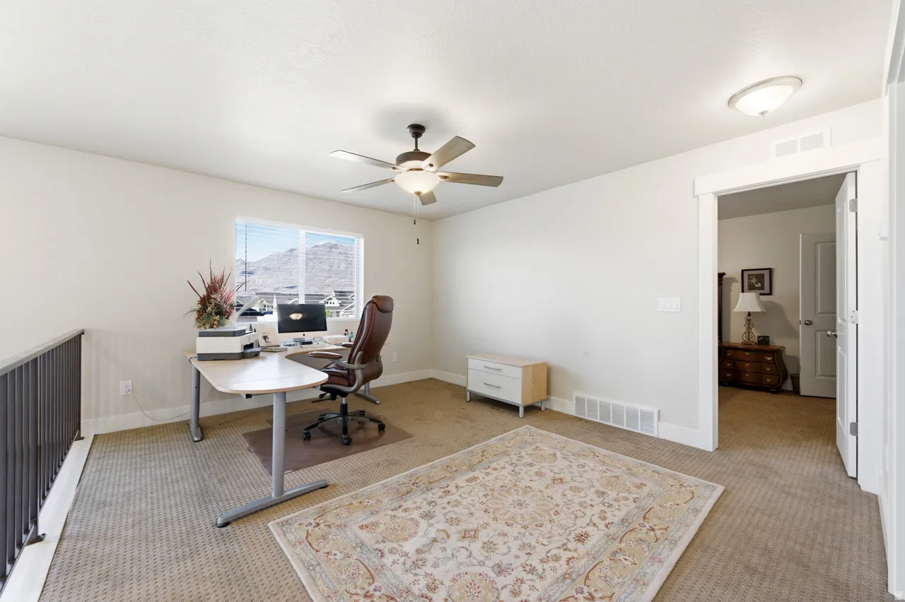 Carpeted home office with a ceiling fan and baseboards