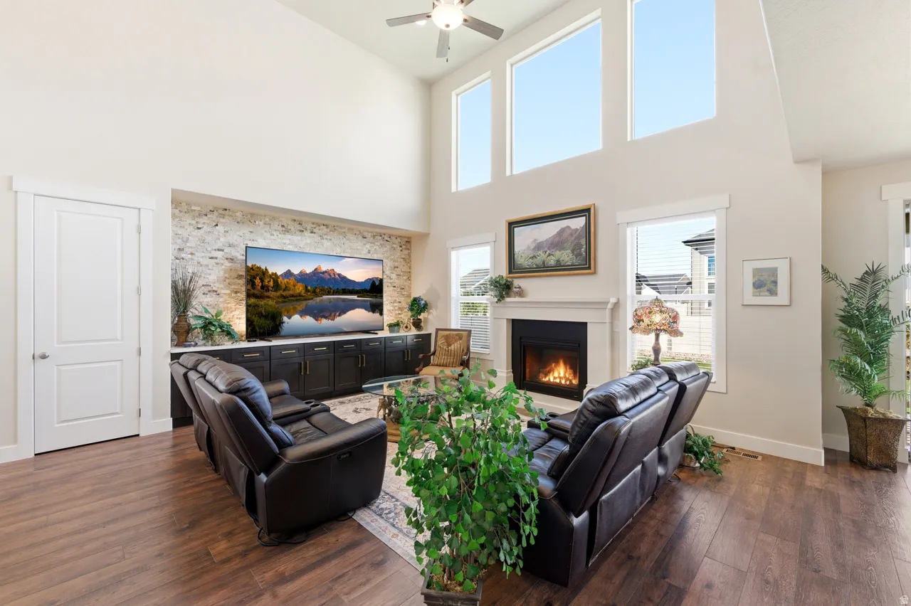 Living area with a glass covered fireplace, dark wood finished floors, a high ceiling, and ceiling fan