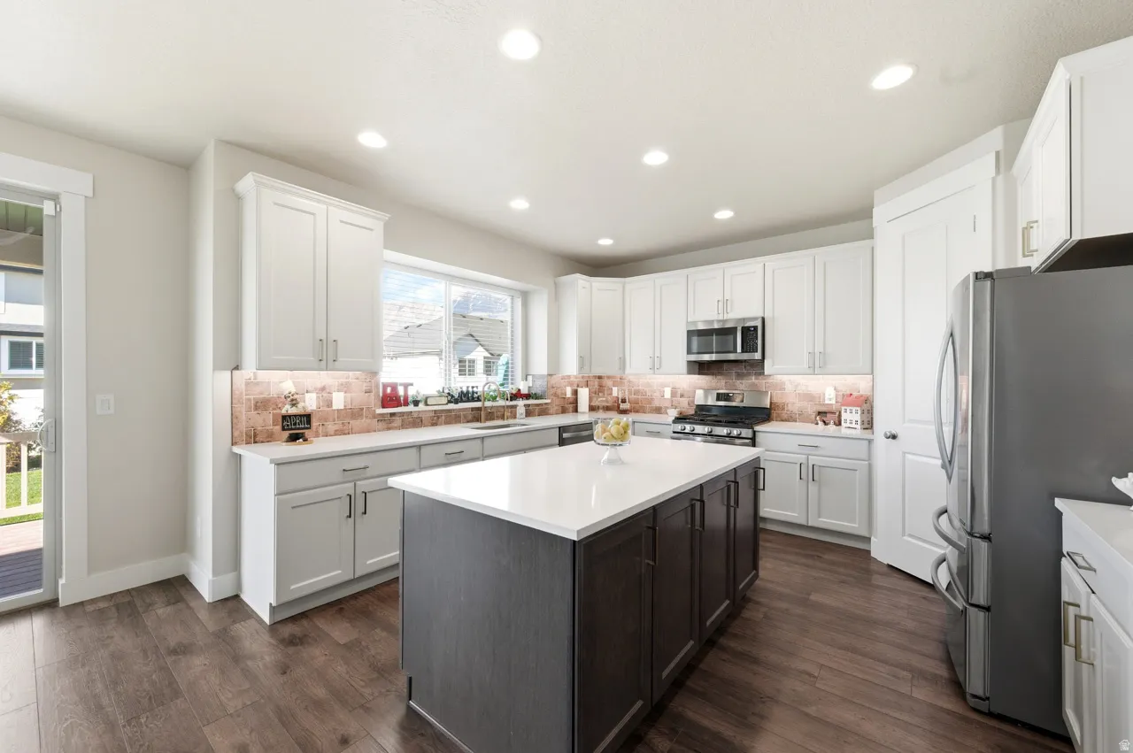 Kitchen featuring stainless steel appliances, a center island, dark wood finished floors, backsplash, and two tone color scheme