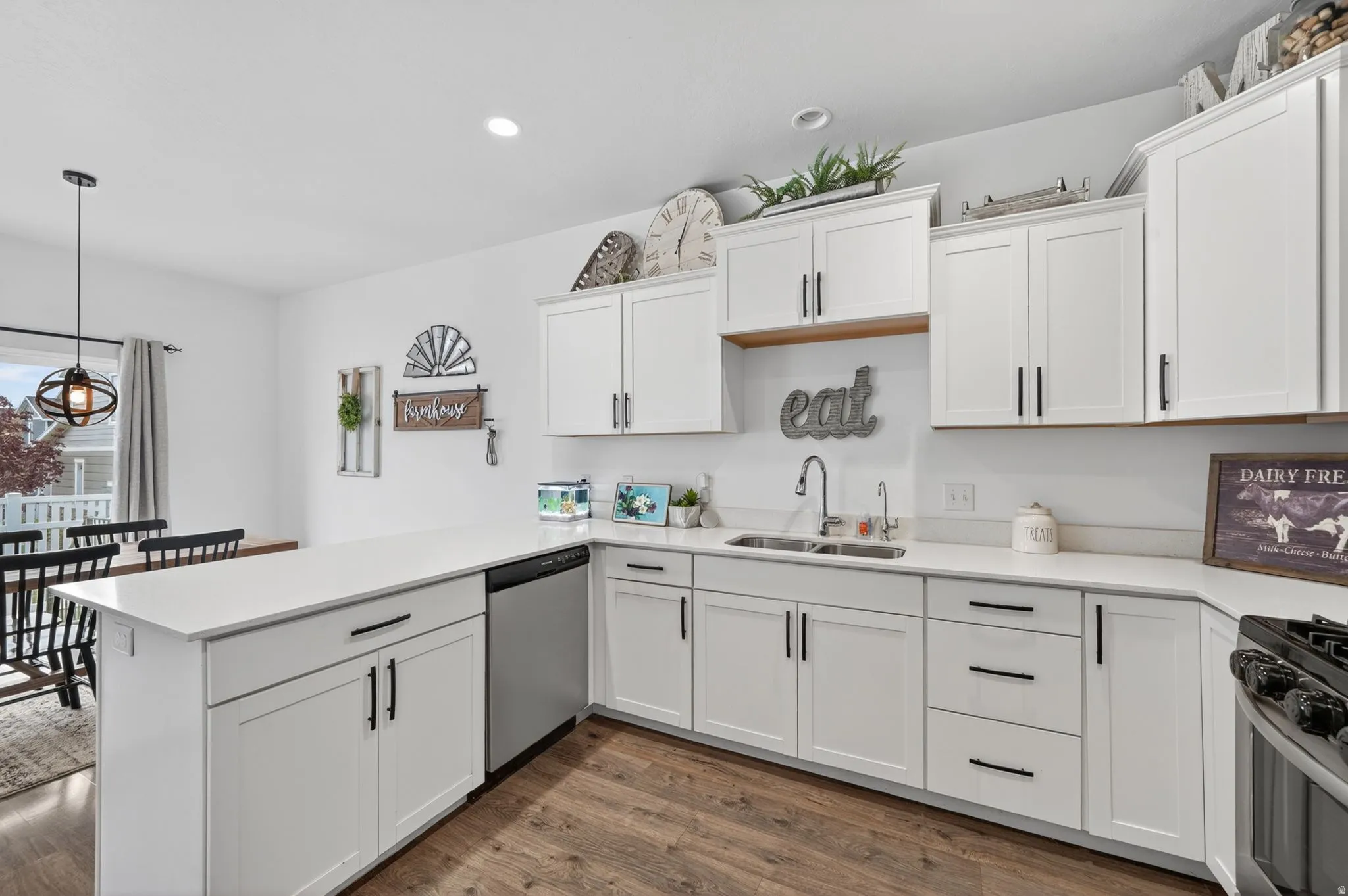 Kitchen with a peninsula, white cabinetry, stainless steel appliances, dark wood-type flooring, and hanging light fixtures