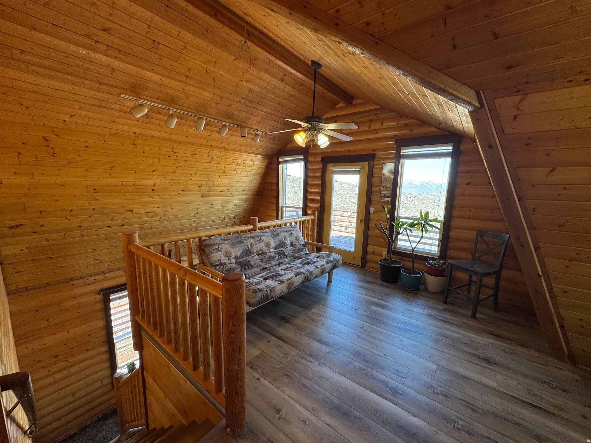 Sitting room with an upstairs landing, rustic walls, hardwood / wood-style floors, track lighting, and lofted ceiling with beams