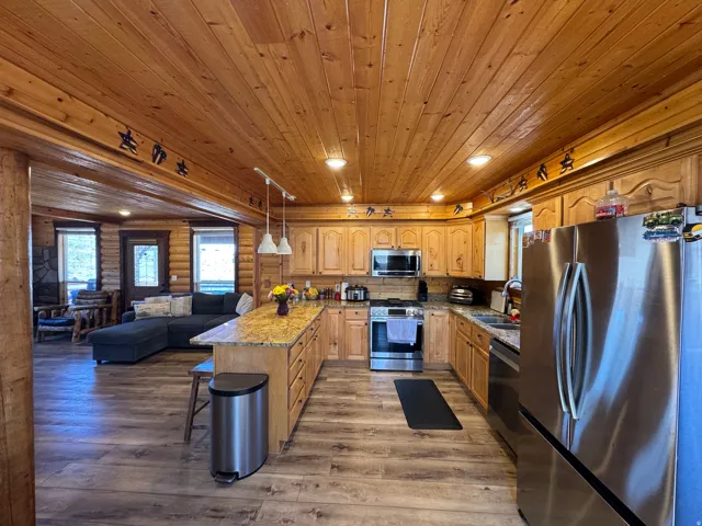 Kitchen with stainless steel appliances, light stone counters, a kitchen bar, open floor plan, and pendant lighting
