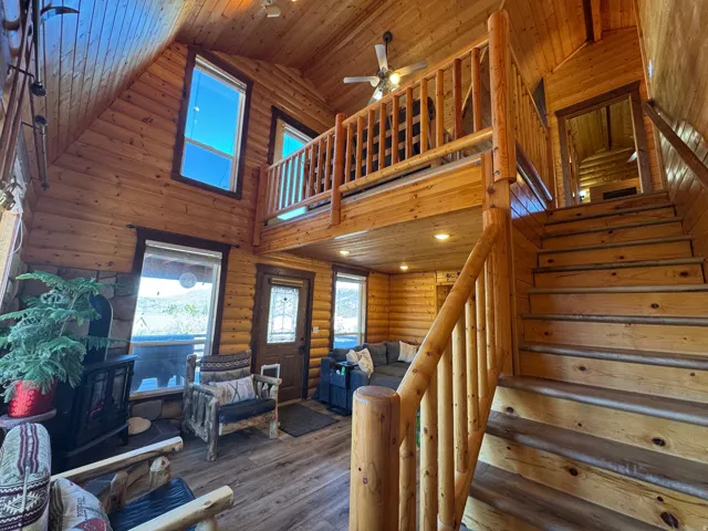 Stairway with a high wooden ceiling, a ceiling fan, log walls, hardwood / wood-style flooring, and a wood stove