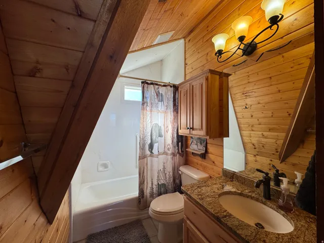 Full bath featuring a vaulted wood ceiling, vanity, wooden walls, and shower / bath combo with shower curtain