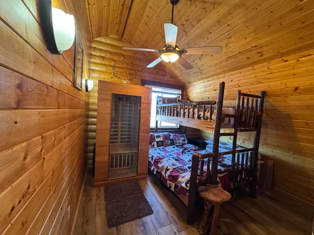 Bedroom featuring a vaulted wooden ceiling, wood-type flooring, a sauna / steam room, rustic walls, and a ceiling fan