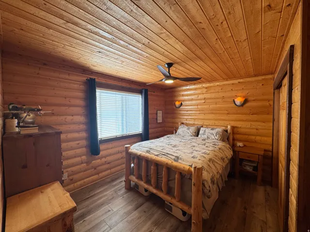 Bedroom featuring rustic walls, dark wood-style floors, and ceiling fan