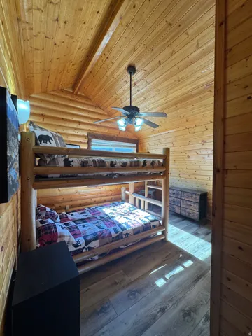 Bedroom featuring wood-type flooring, log walls, and a wooden ceiling with exposed beams