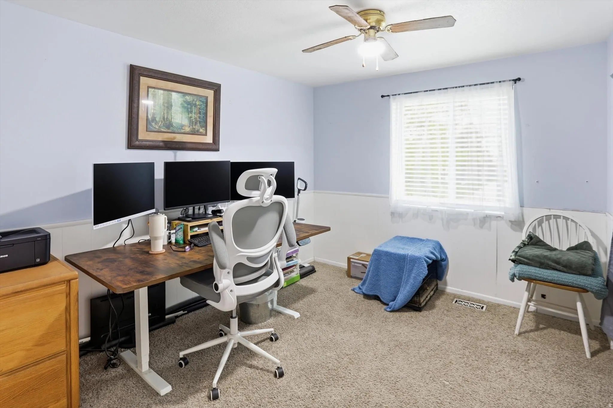 Office area with light colored carpet, a wainscoted wall, and a ceiling fan