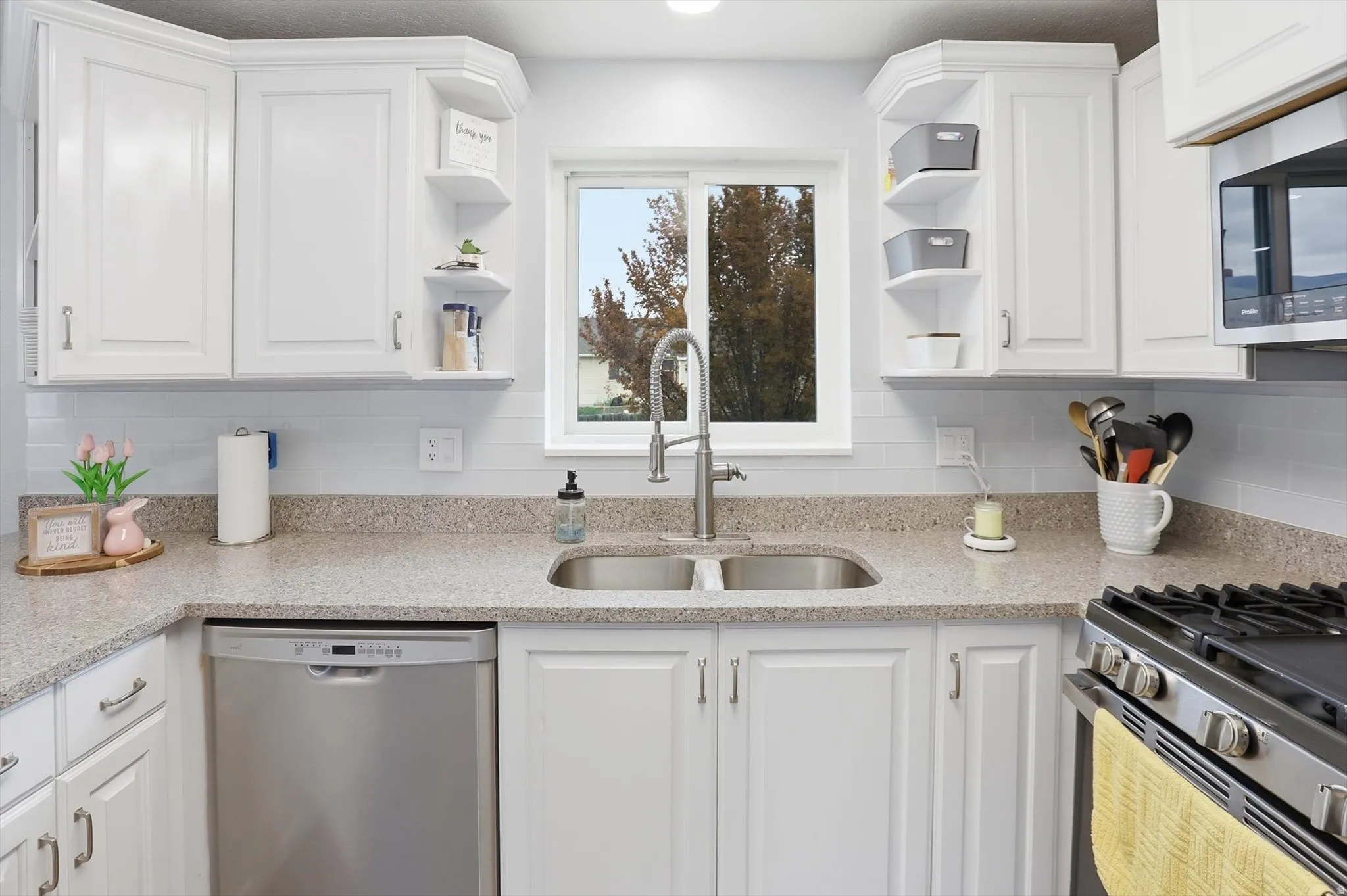 Kitchen featuring white cabinetry, open shelves, light stone countertops, stainless steel appliances, and backsplash