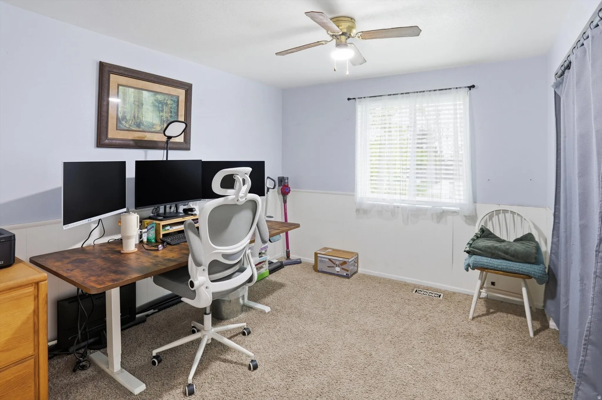 Office with light carpet, a ceiling fan, and a wainscoted wall