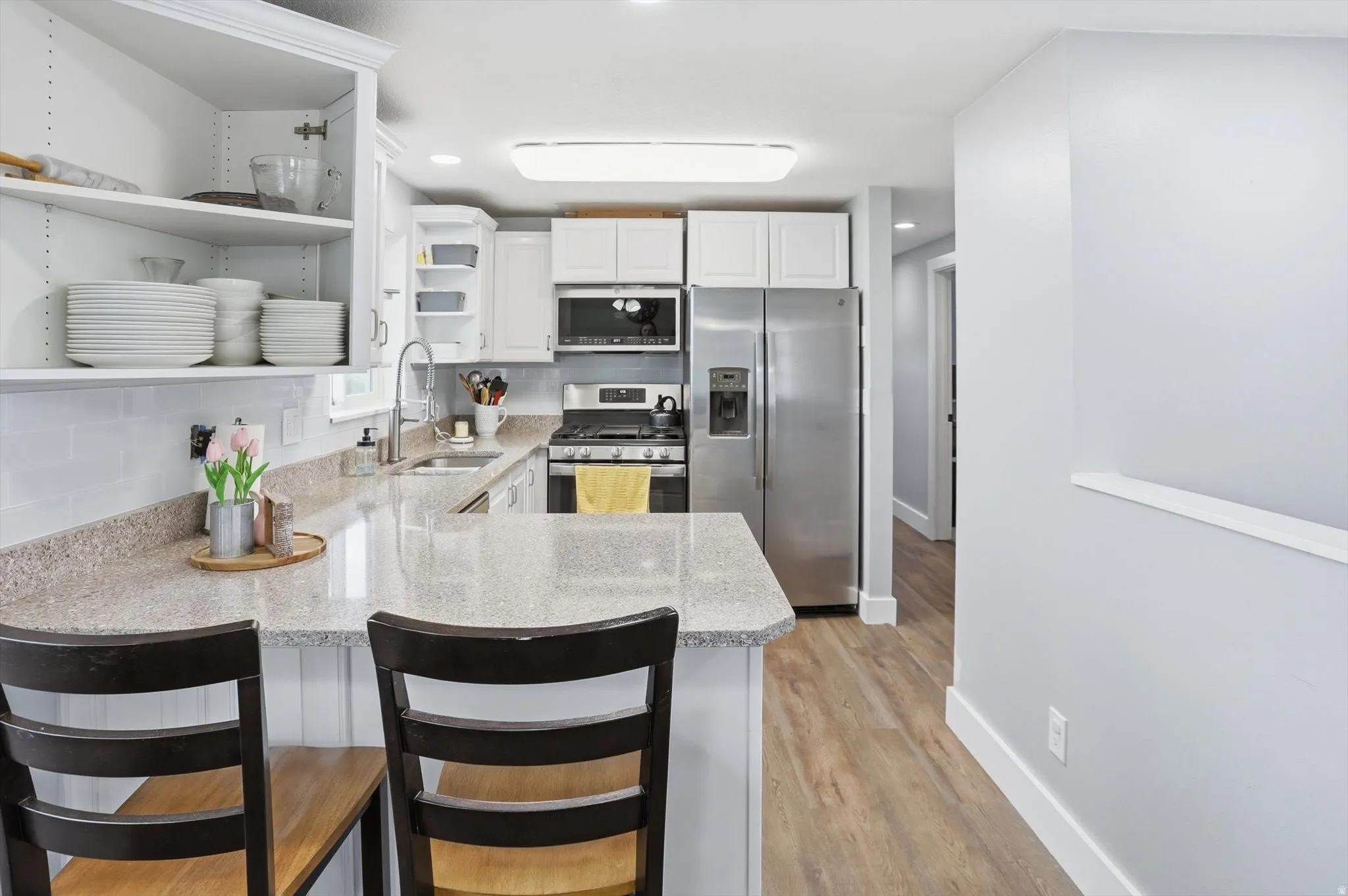 Kitchen featuring open shelves, stainless steel appliances, white cabinets, a peninsula, and light wood-type flooring