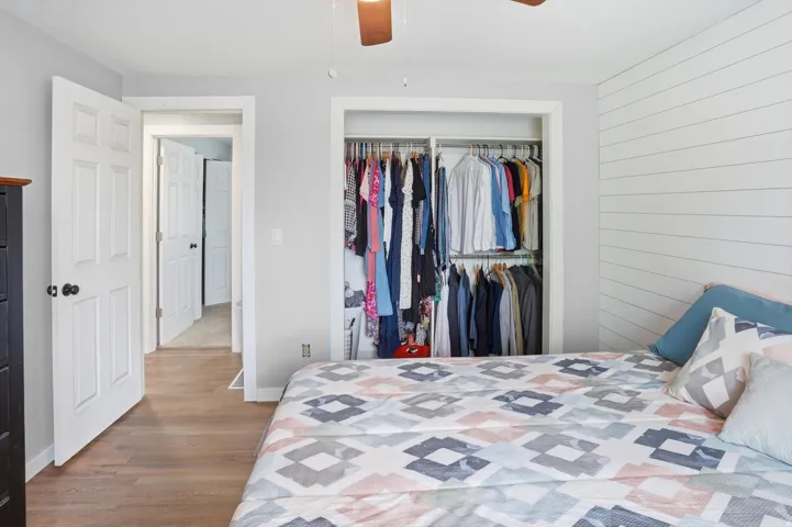 Bedroom with a closet, wood finished floors, ceiling fan, and wood walls