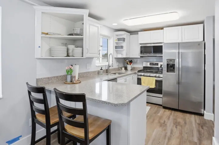 Kitchen featuring stainless steel appliances, open shelves, a kitchen bar, a peninsula, and white cabinets