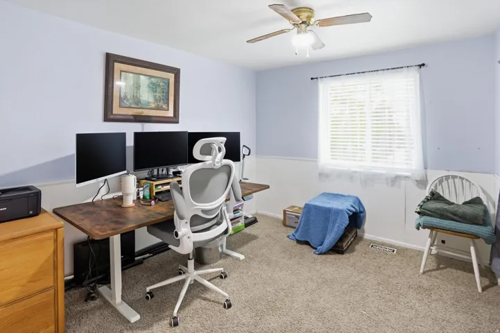 Office area with light colored carpet, a wainscoted wall, and a ceiling fan
