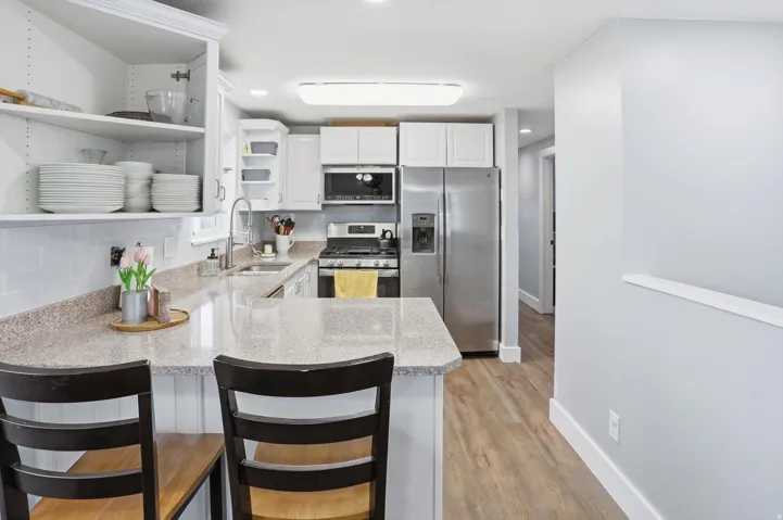 Kitchen featuring open shelves, stainless steel appliances, white cabinets, a peninsula, and light wood-type flooring