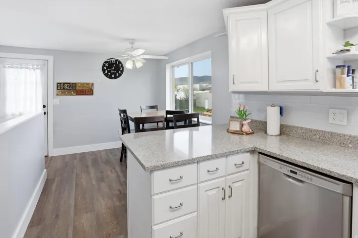 Kitchen featuring stainless steel dishwasher, white cabinetry, open shelves, a peninsula, and decorative backsplash