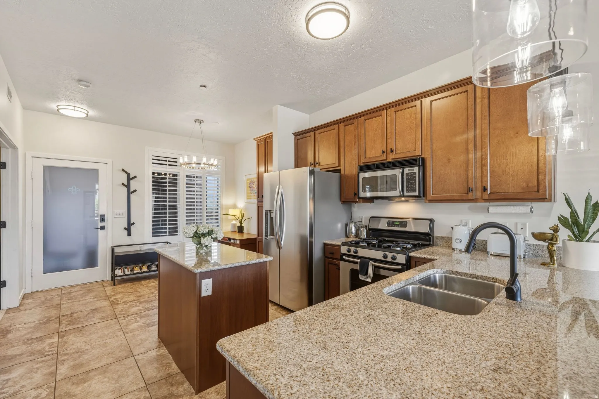 Kitchen with a center island, stainless steel appliances, wood finish cabinets, light stone counters, and suspended lighting