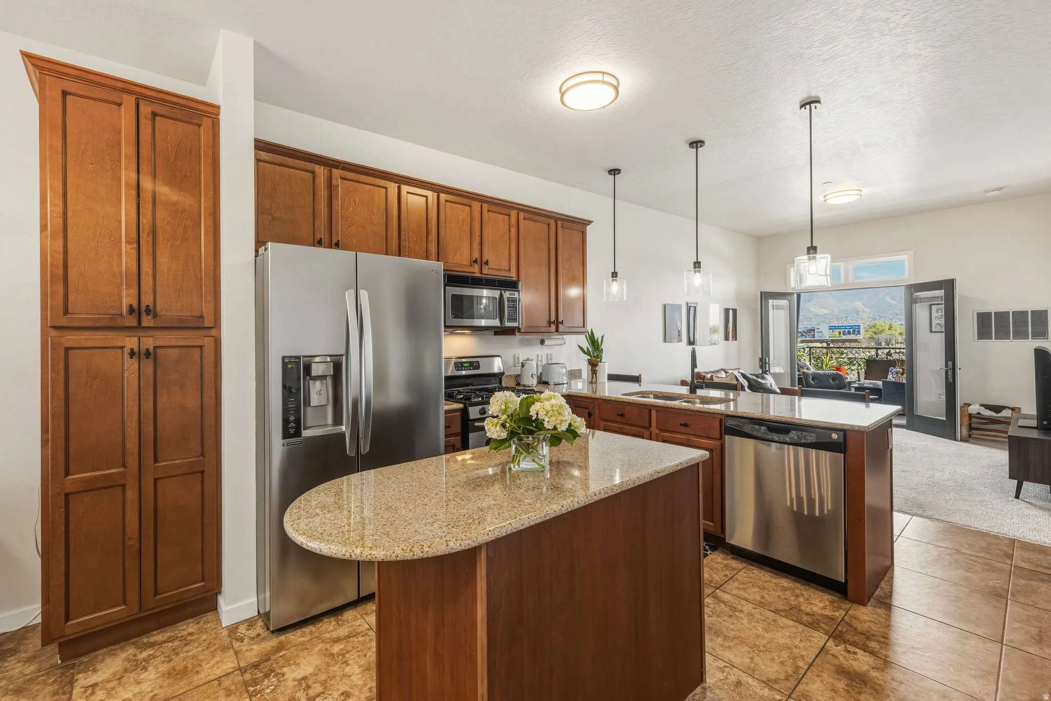 Kitchen featuring stainless steel appliances, a peninsula, hanging light fixtures, a center island, and light stone counters