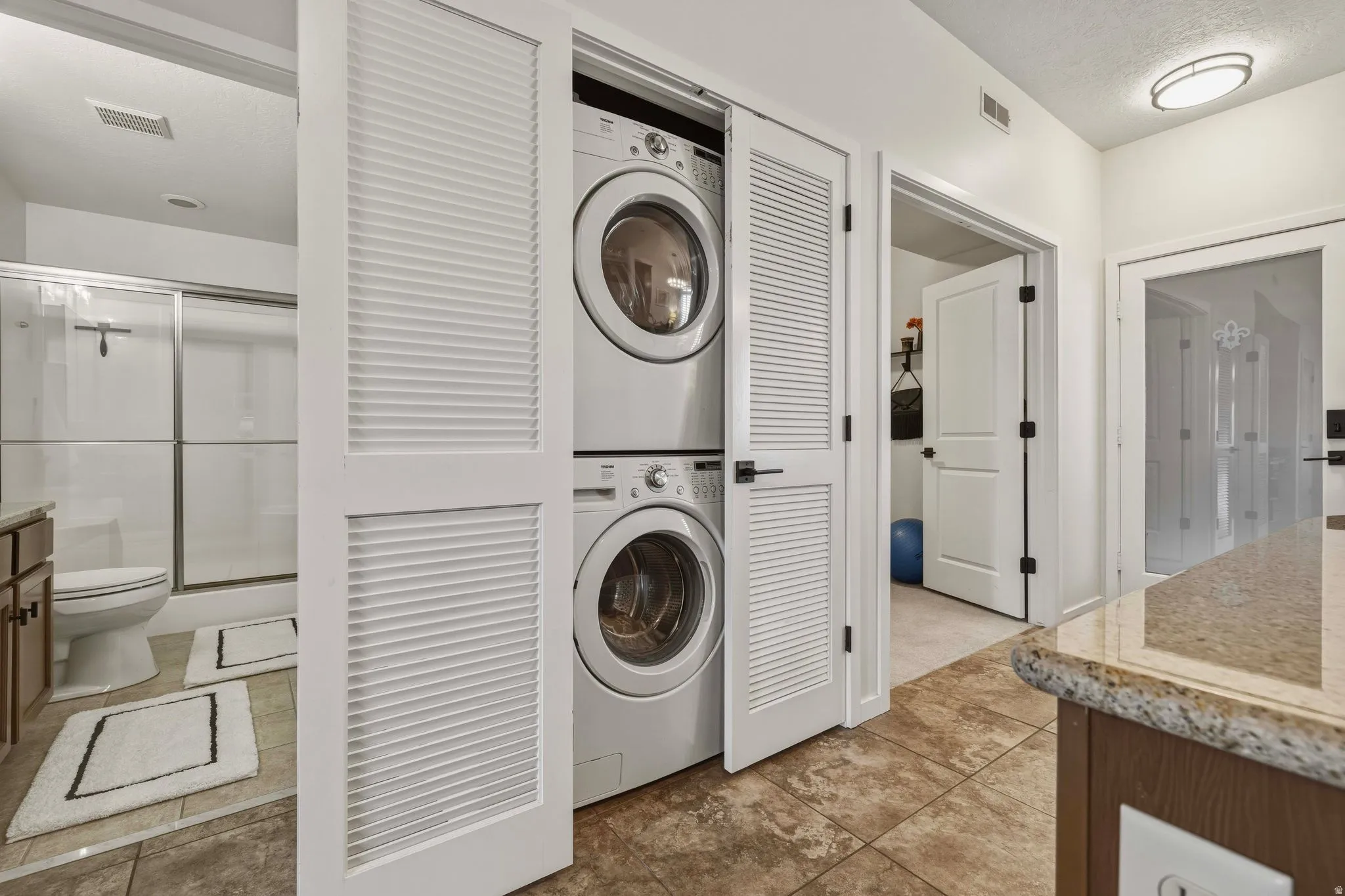Laundry area with stacked washing machine and dryer and a textured ceiling