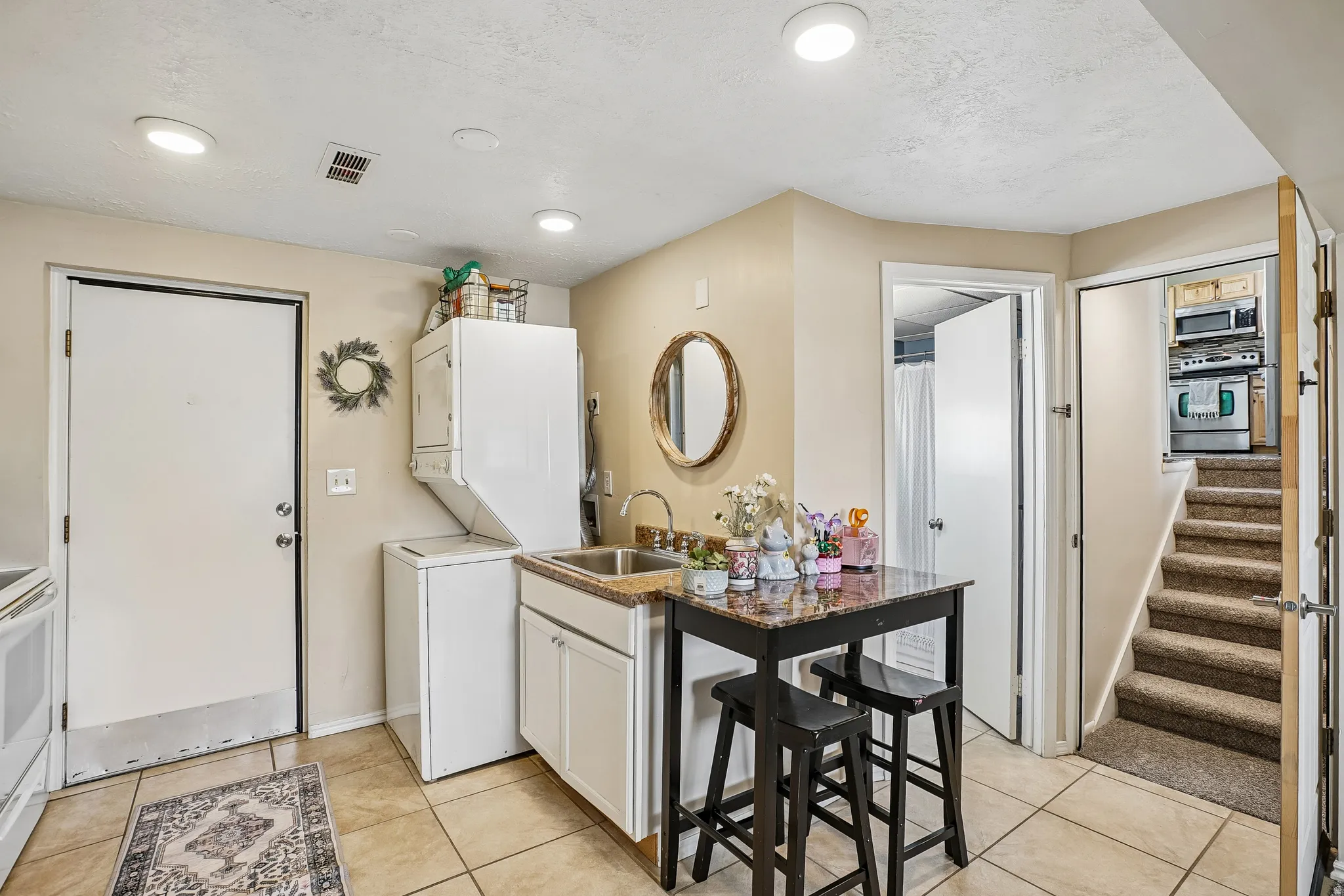 Kitchen with white cabinets, stainless steel appliances, stacked washer and clothes dryer, light tile patterned flooring, and light countertops