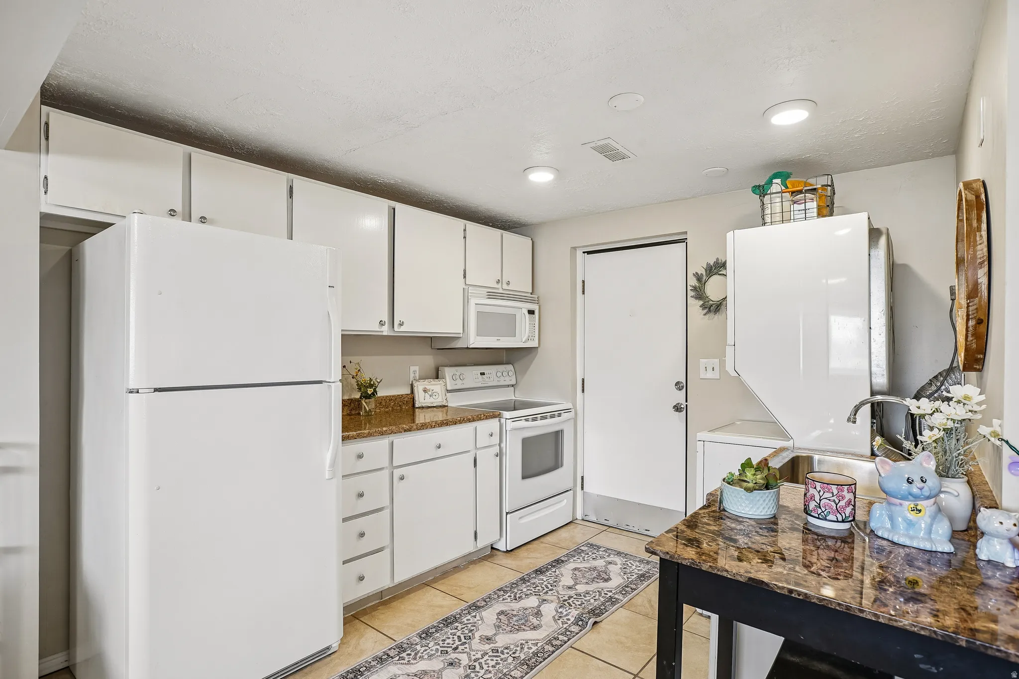 Kitchen with white appliances, white cabinets, light tile patterned floors, dark stone counters, and recessed lighting