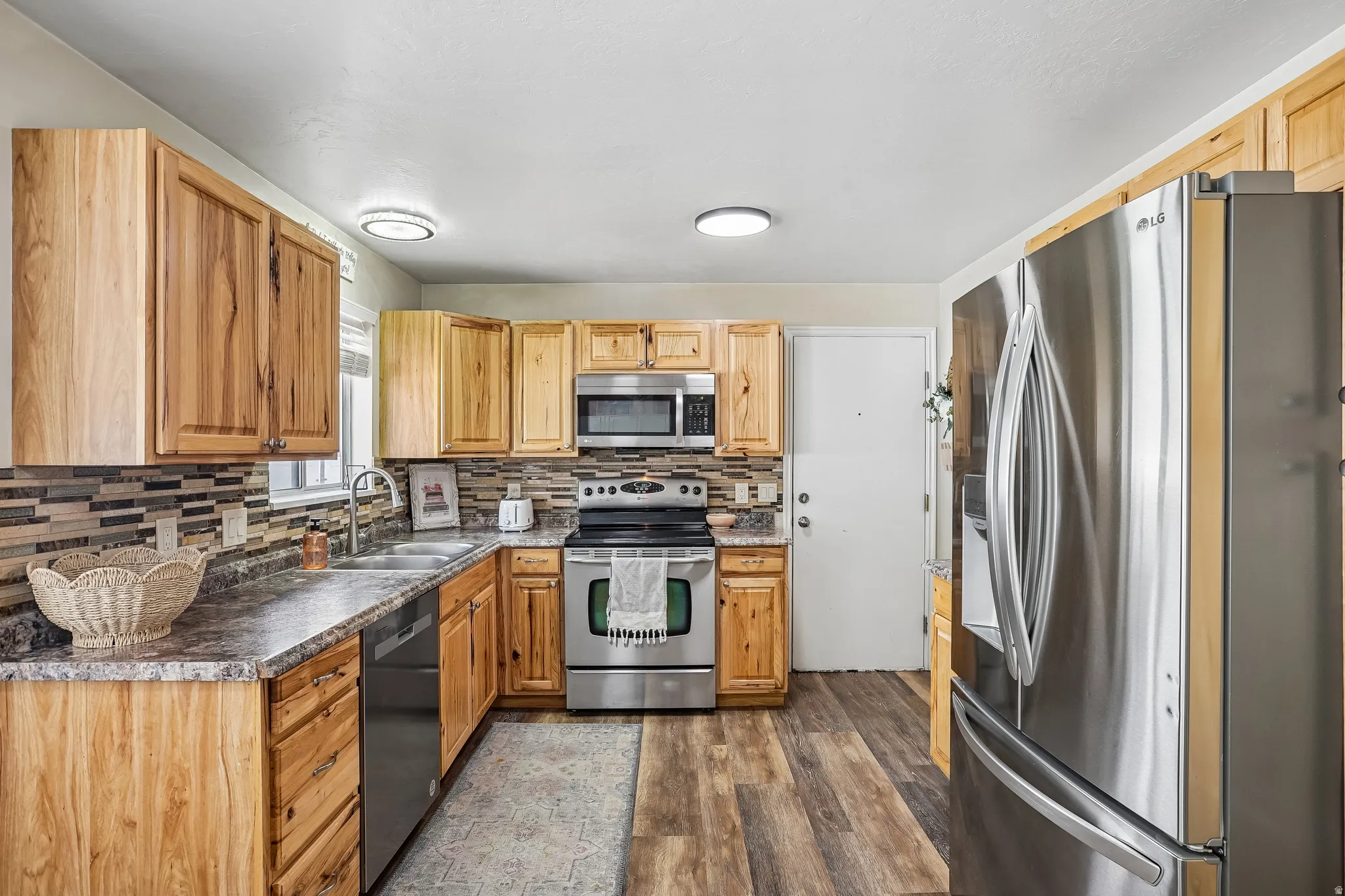 Kitchen featuring stainless steel appliances, dark countertops, dark wood-type flooring, and tasteful backsplash