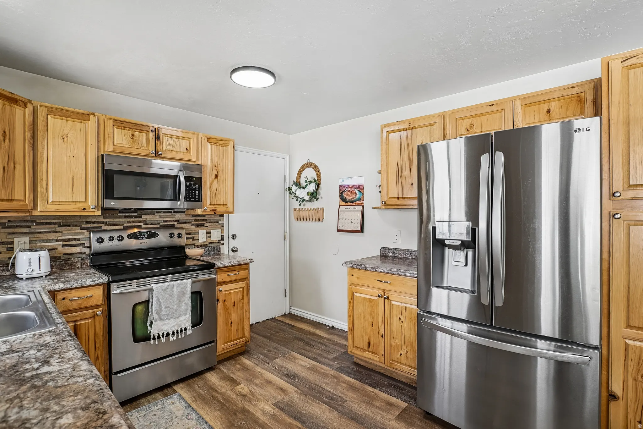 Kitchen featuring stainless steel appliances, dark wood-type flooring, and backsplash