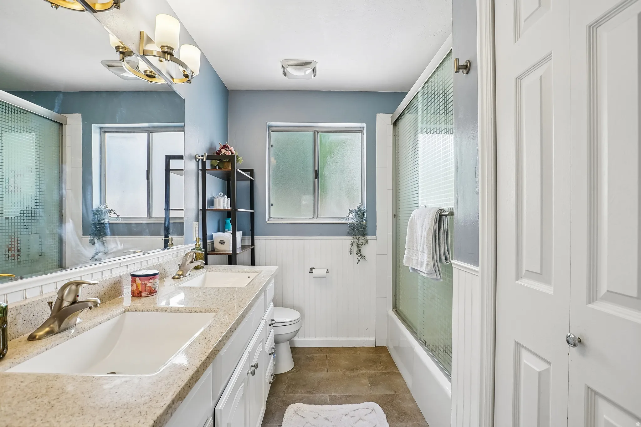 Bathroom with a wainscoted wall, double vanity, and bath / shower combo with glass door