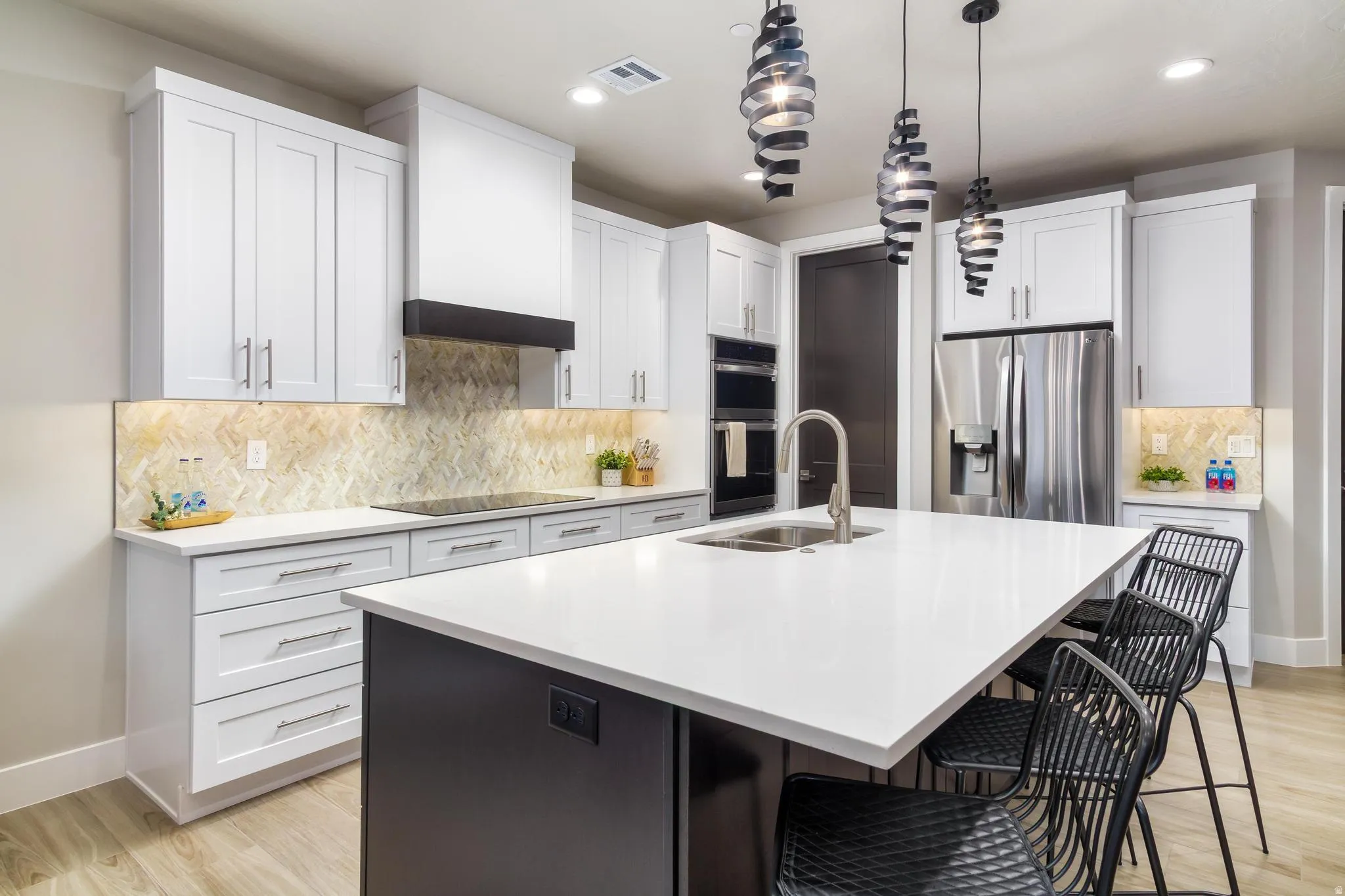 Kitchen featuring a breakfast bar, stainless steel appliances, a kitchen island with sink, light wood-style floors, and two tone cabinets