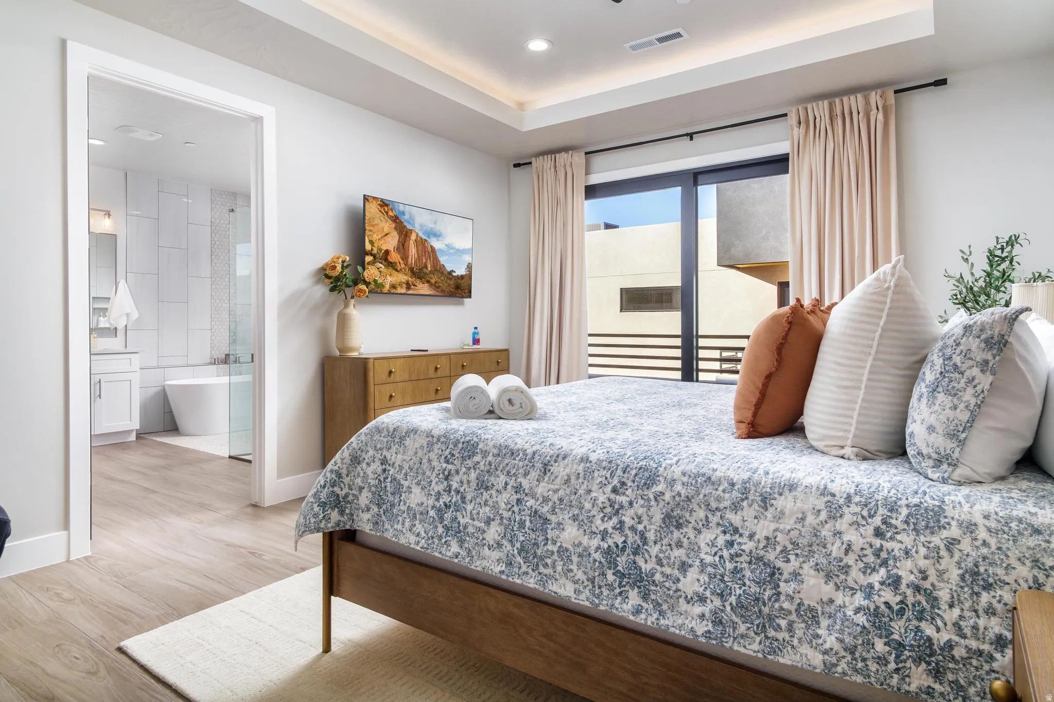 Bedroom featuring access to exterior, a raised ceiling, light wood-style floors, recessed lighting, and connected bathroom