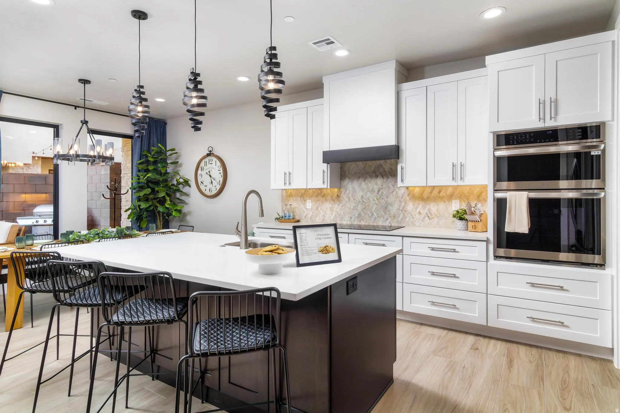 Dual tone kitchen featuring light wood-type flooring, a kitchen bar, stainless steel double oven, dual tone cabinets, and a kitchen island with sink