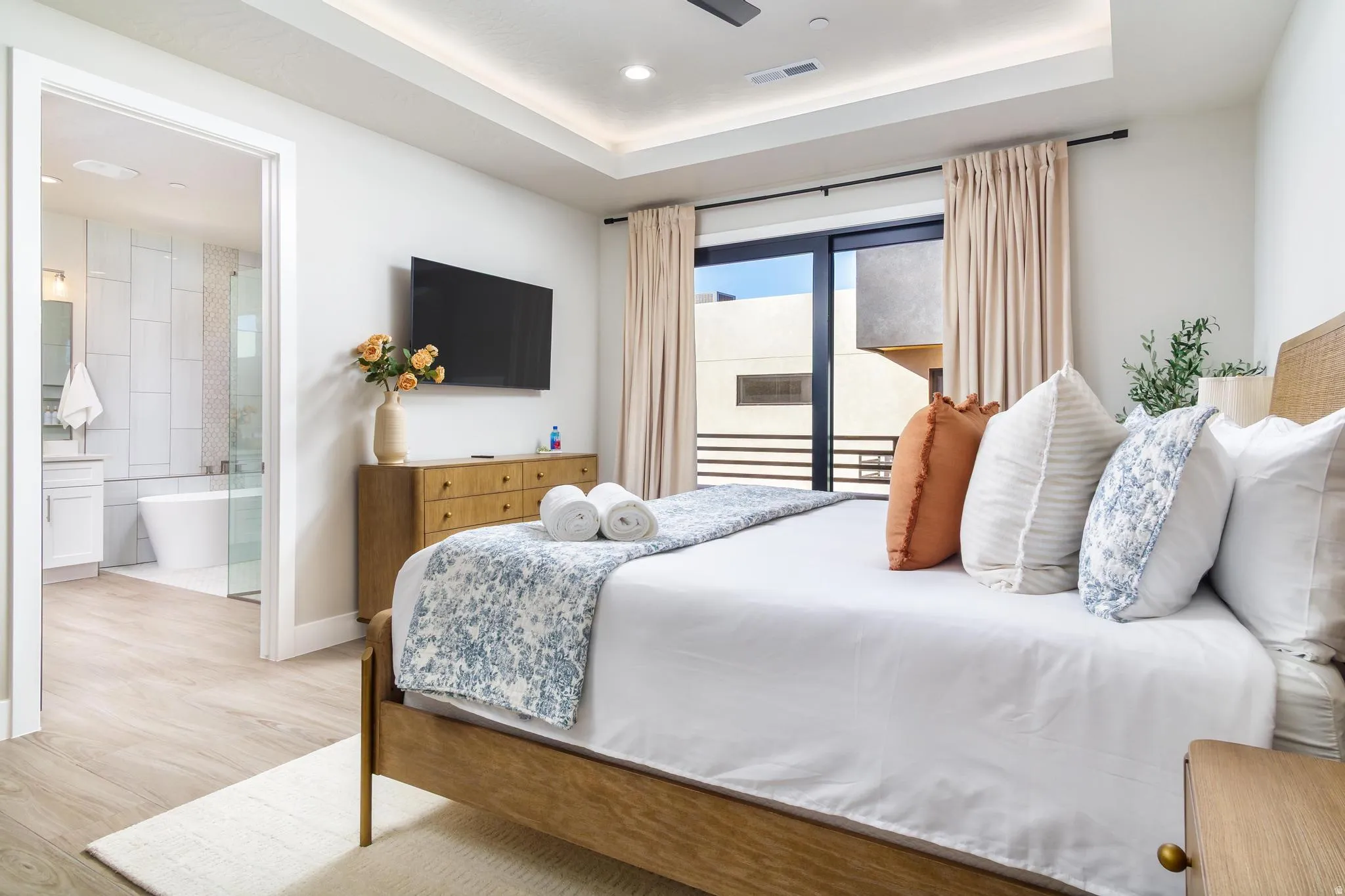 Bedroom with light wood-style flooring, a tray ceiling, ceiling fan, access to exterior, and connected bathroom