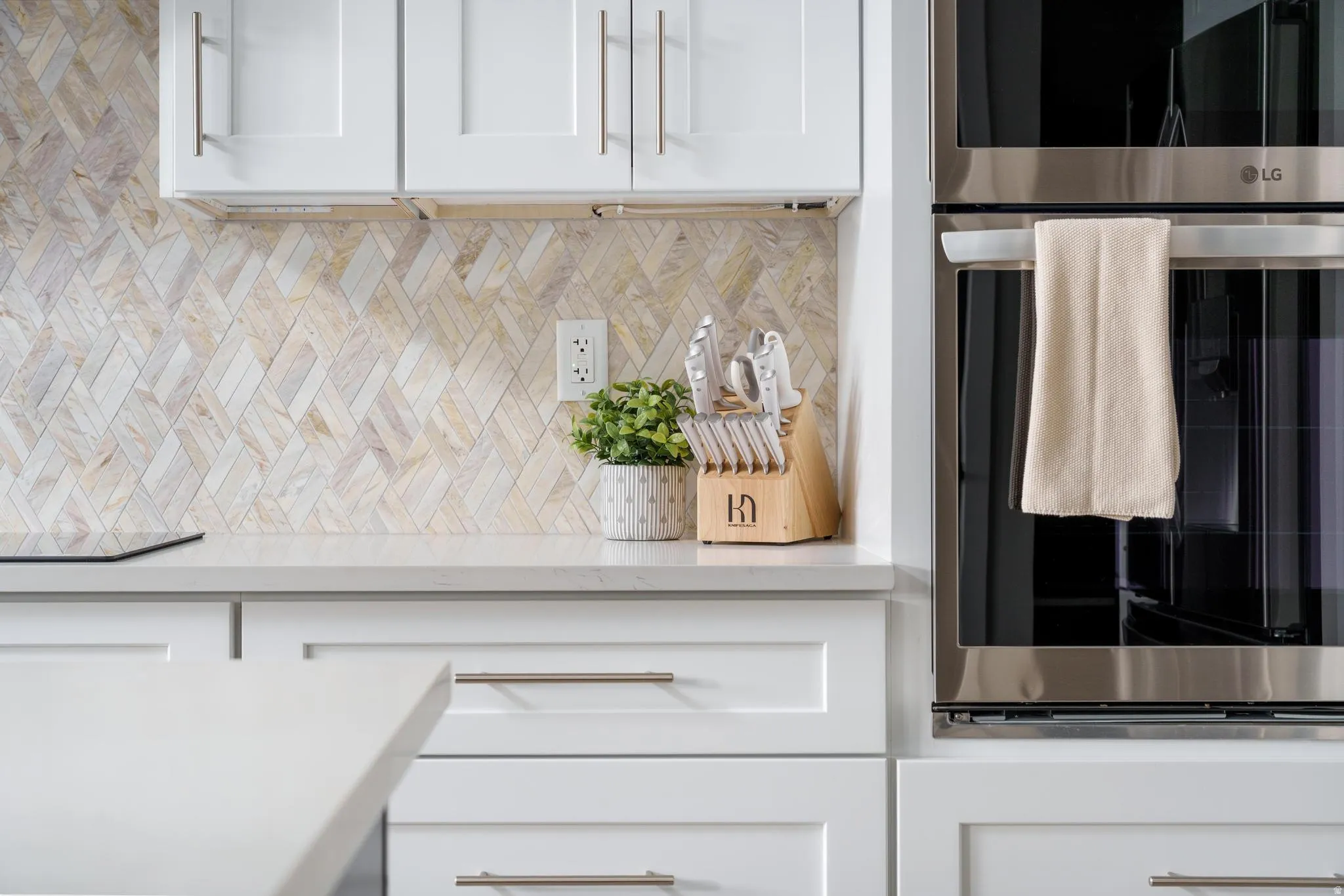 Kitchen view of white cabinets, light stone countertops, double oven, and decorative backsplash