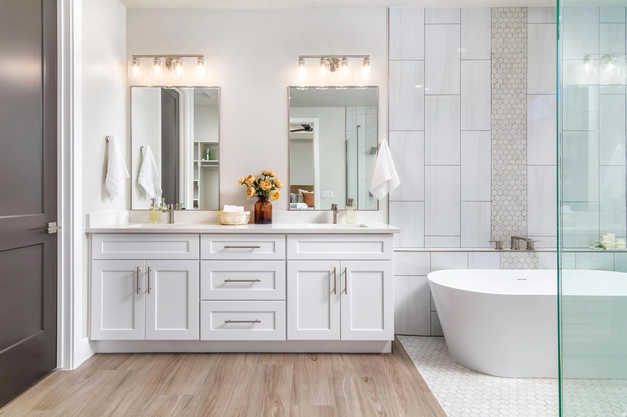 Bathroom featuring double vanity, a soaking tub, tile walls, a shower with door, and light wood-style flooring