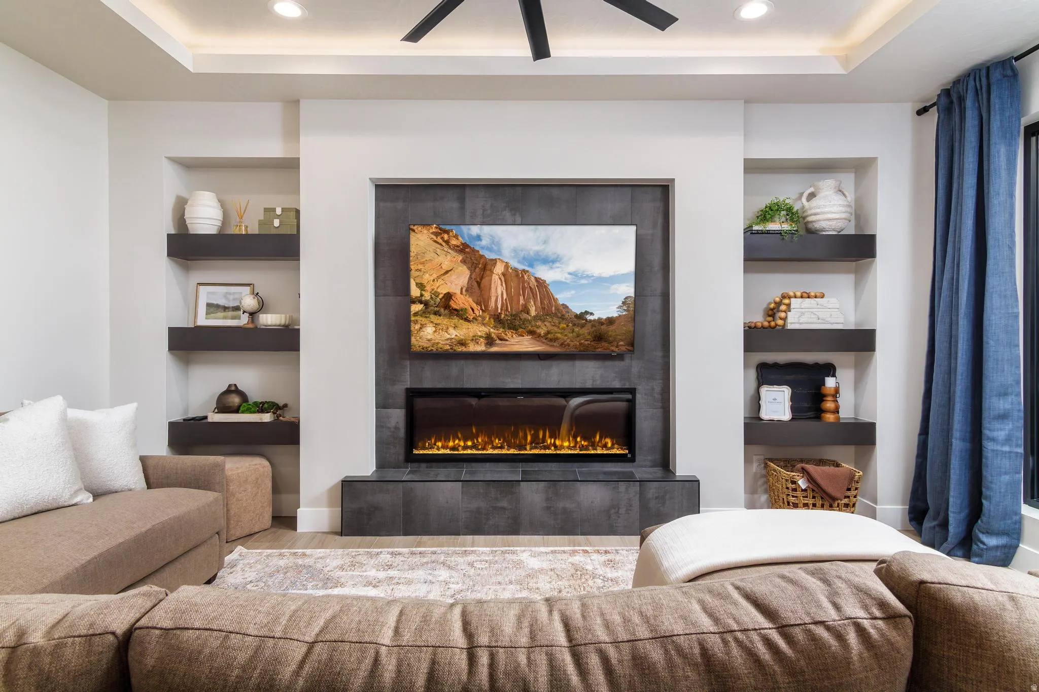 Living room with built in features, wood finished floors, a fireplace, a tray ceiling, and ceiling fan