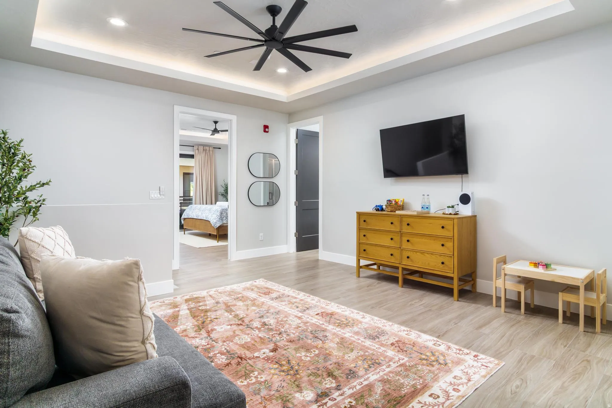 Living room with light wood finished floors, a tray ceiling, recessed lighting, and a ceiling fan