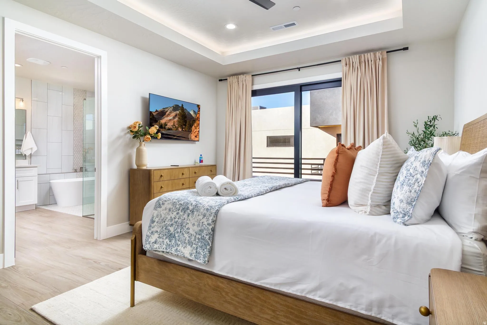 Bedroom with light wood-style floors, a raised ceiling, ceiling fan, access to outside, and ensuite bathroom