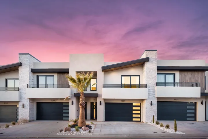 Modern home with a balcony, stucco siding, an attached garage, and driveway