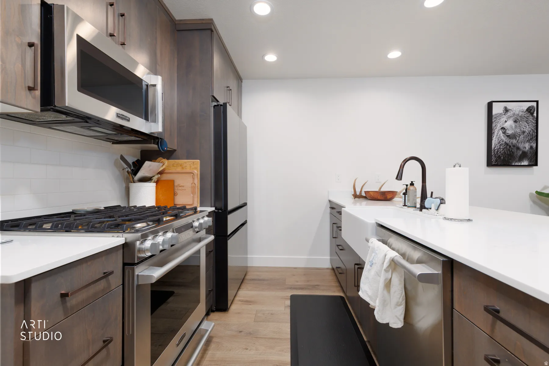 Kitchen featuring stainless steel appliances, dark wood finish cabinetry, light wood-style flooring, light stone counters, and recessed lighting