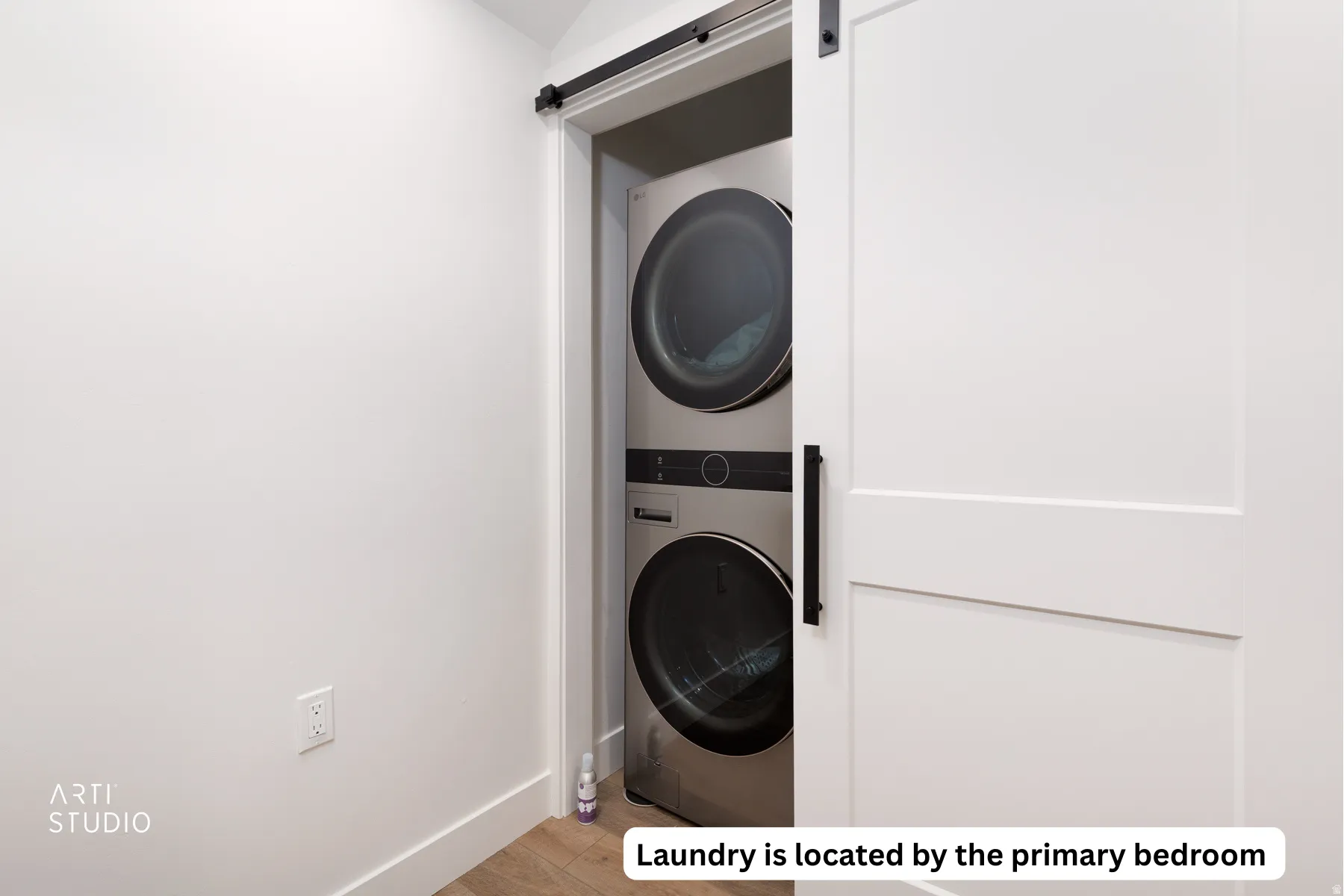 Laundry area with a barn door, stacked washer and clothes dryer, and light wood-type flooring