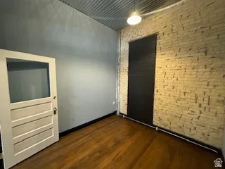 Empty room featuring dark wood finished floors and brick wall