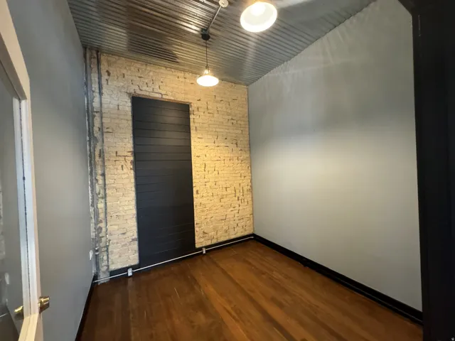 Unfurnished room with brick wall and dark wood-style flooring